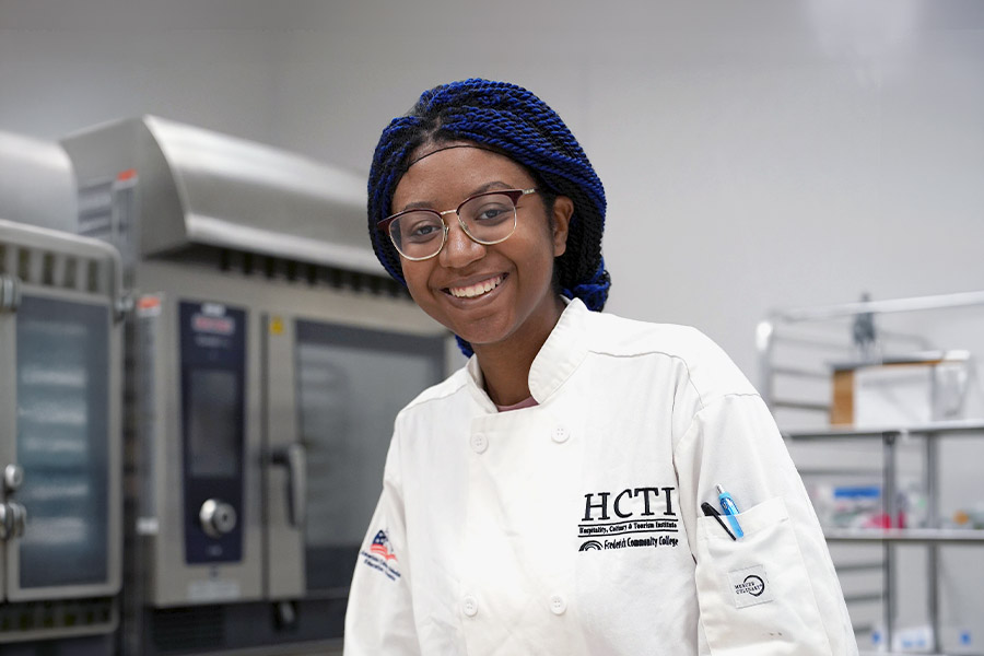 HCTI culinary student in white chef coat smiling in a commercial kitchen